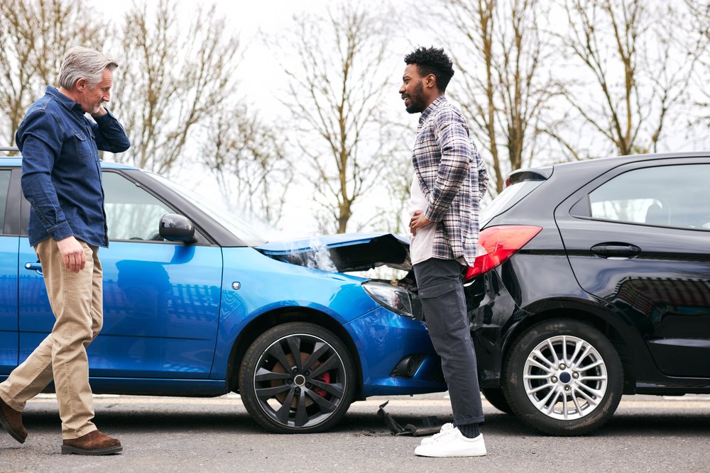 Two drivers standing outside of their cars after a rear end collision, which may result in a settlement for the driver who got rear-ended.