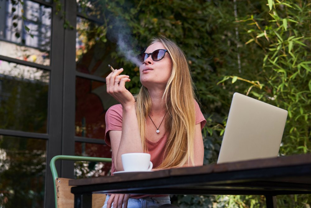 Una mujer fumando marihuana al aire libre mientras está sentada en un café.
