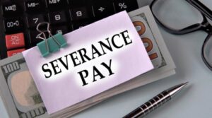 A stack of one hundred dollar bills sits on a typical office desktop. There is a note attached to the money that reads "severance pay".