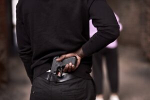 Man in a dark alley about to take out a gun in a prelude to an assault with a deadly weapon