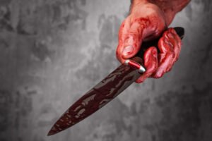 Mano sangrienta sosteniendo un cuchillo sangriento tras una batería con un arma mortal