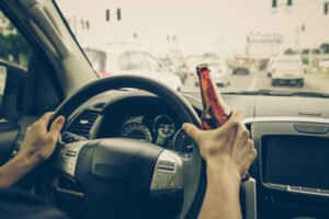 Manos en el volante sosteniendo una botella de cerveza