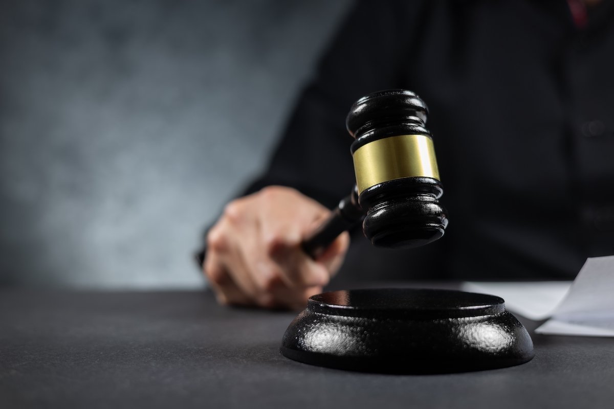 Judge hammering down a wooden gavel on his desk against a grey background