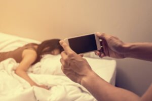 Hombre sosteniendo un teléfono para fotografiar a una mujer en la cama como chantaje en violación de NRS 205.320 