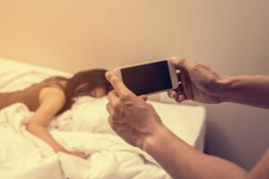 Hombre sosteniendo el teléfono para fotografiar a una mujer en la cama como chantaje en violación de NRS 205.320 