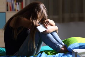 Teen girl on bed holding her phone in despair