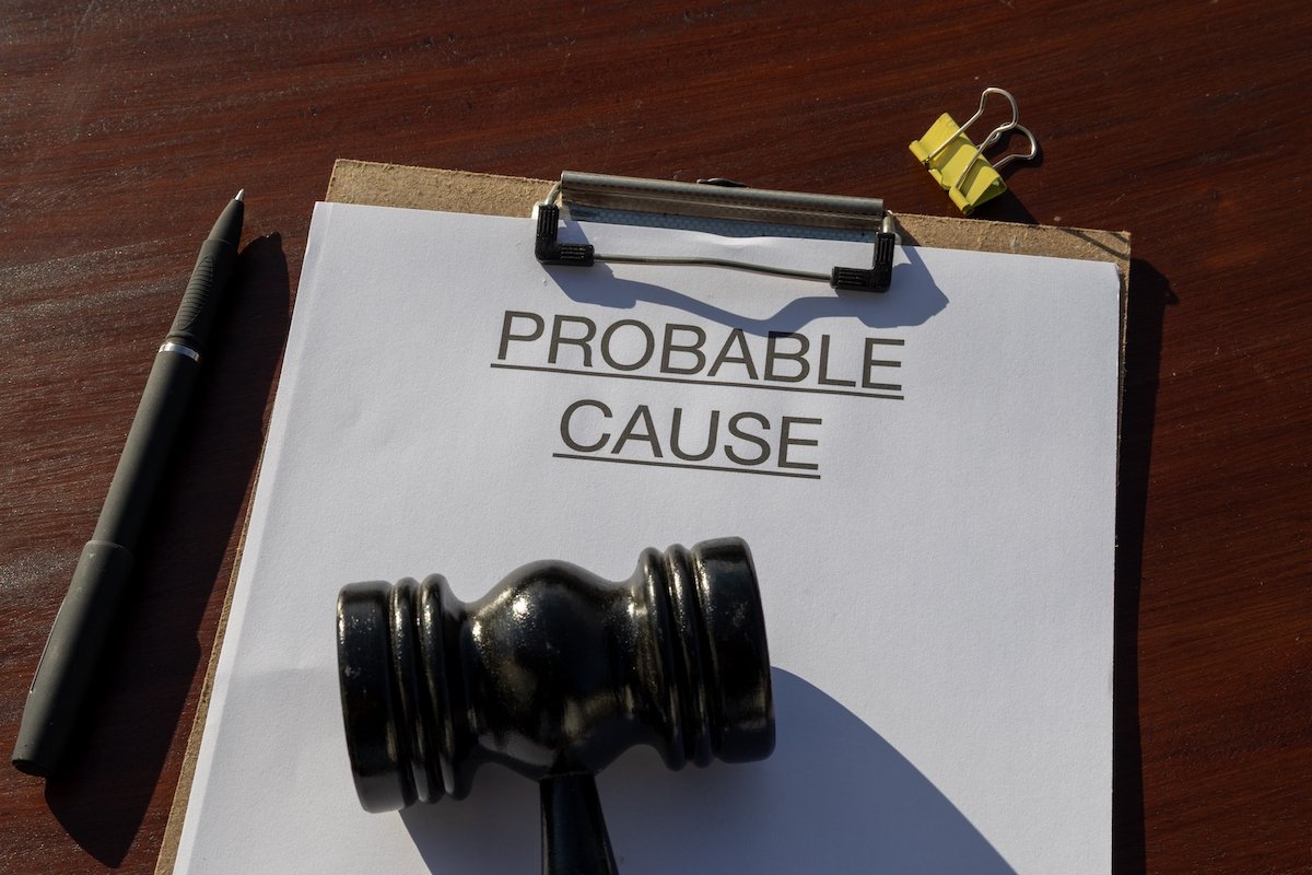 Clipboard that says "probable cause" above a gavel on a wooden desk