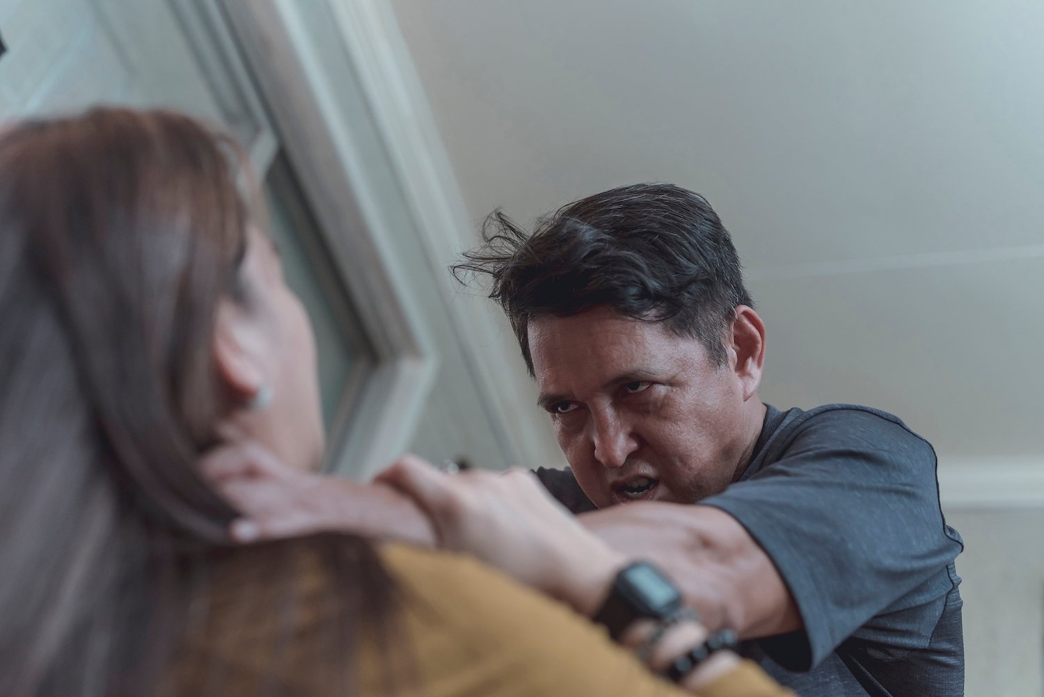 En una sala, un hombre estrangulando a una mujer con rabia mientras ella intenta detenerlo