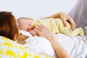 Baby resting on belly of new mother in bed while on maternity leave