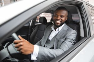 Hombre feliz en traje de negocios conduciendo su sedán durante un viaje de trabajo