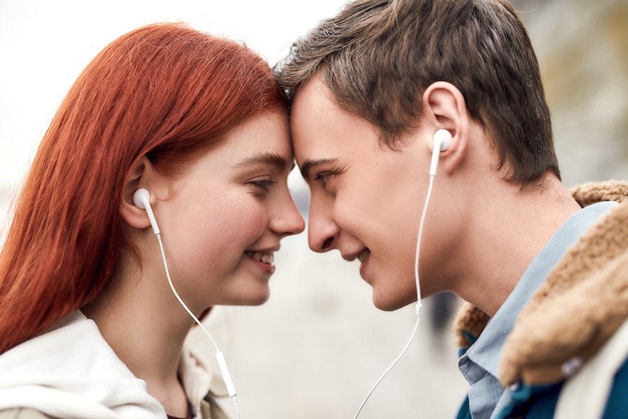 Young smiling teenage couple touching foreheads while listening on their headphones