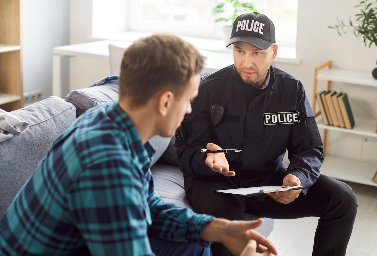 Oficial de policía hablando con una víctima masculina en su sala de estar