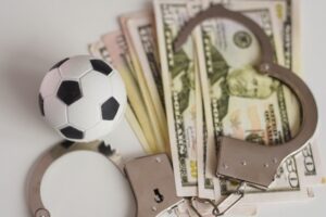 handcuffs, dinero y un balón de fútbol, ilustrando el soborno deportivo en violación de NRS 207.290