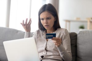 Mujer con tarjeta de crédito mirando su computadora desconcertada después de que su compra sea rechazada