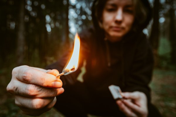 Persona joven encendiendo un fósforo en un bosque al atardecer