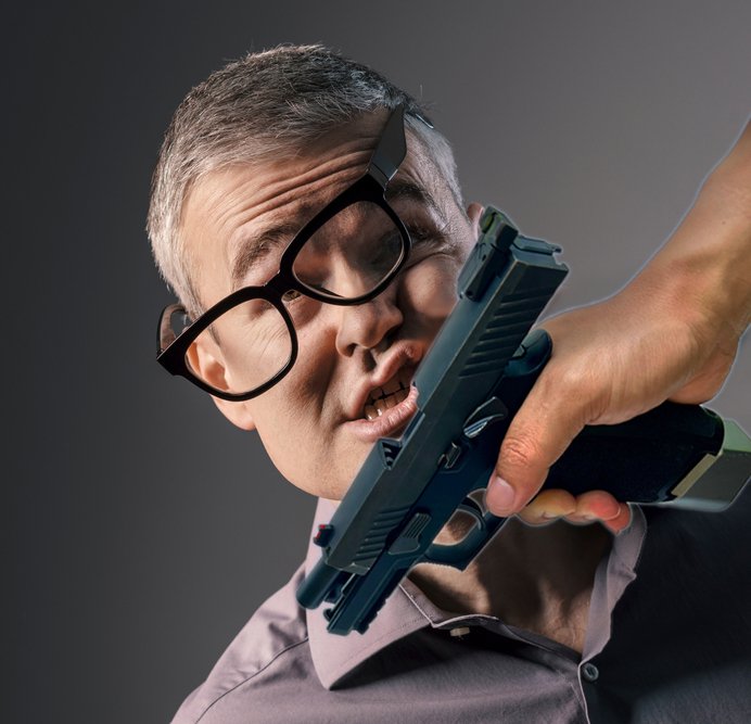Middle-aged caucasian man with gray hair has his glasses knocked off and his face contorted as he is violently impacted by a gun being held in another man's hand