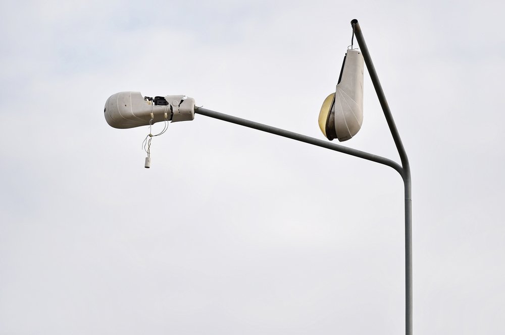View of two broken streetlights hanging loosely by wires on metal poles, with grey sky in background