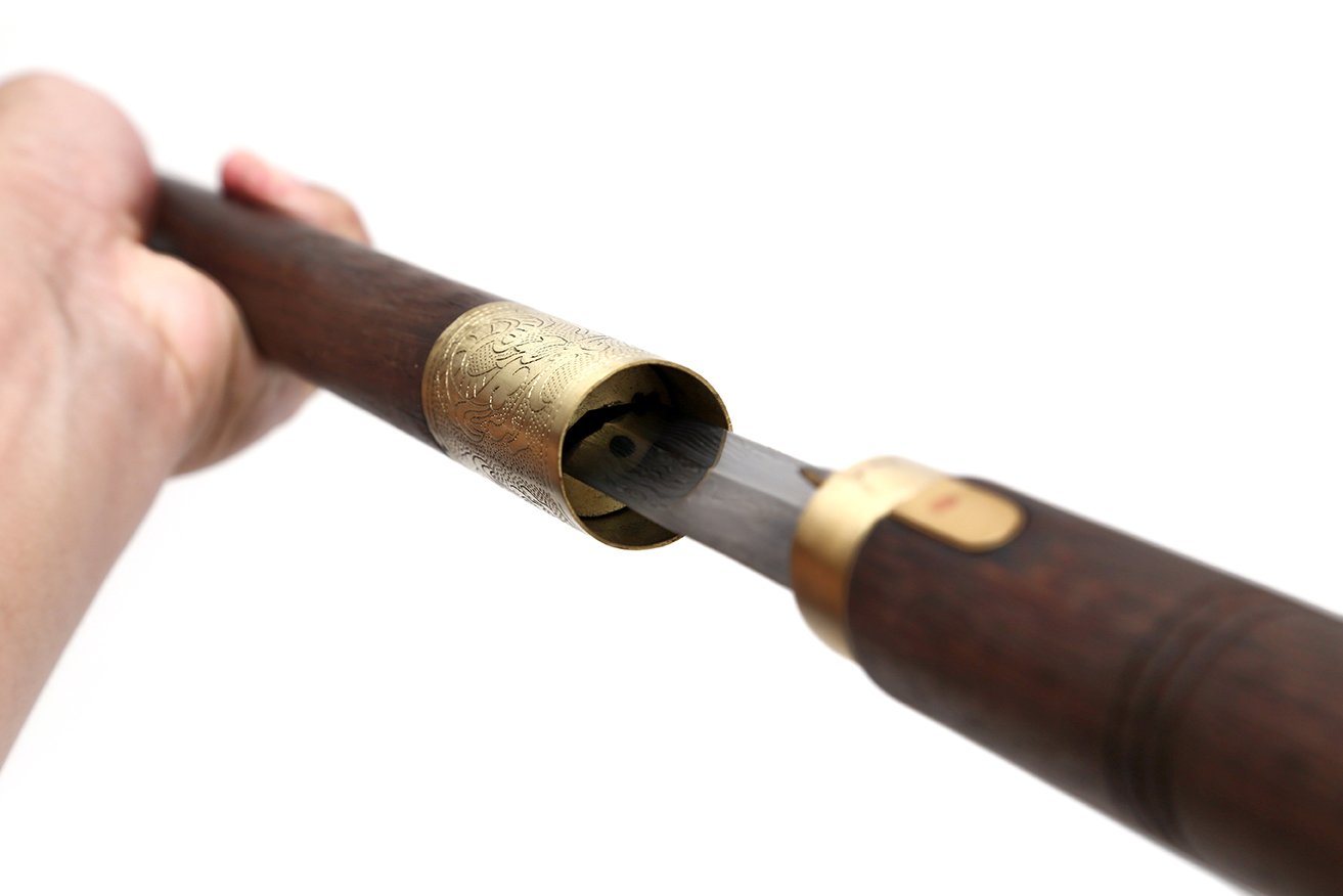 A man's hand grips the top of a shobi-zue, pulling the cane open to reveal a hidden sharp metal object inside