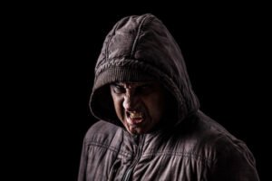 Angry, snarling man in a hooded jacket making criminal threats against a black background