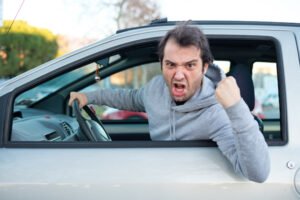 An angry man in a hoodie leaning out the driver's side window of his car and pumping his fist while making a criminal threat in violation of PC 422