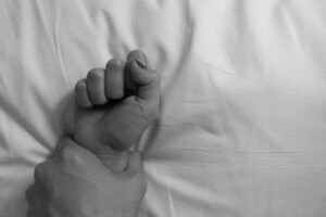 Mano masculina sosteniendo la mano femenina en la cama