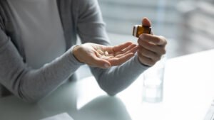 Primer plano de una mujer dispensando una pastilla sedante de una botella en su palma sobre una mesa