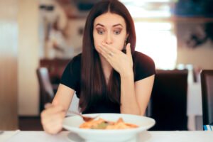 Mujer comiendo en restaurante mientras sostiene su mano sobre su boca con disgusto