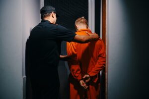 Prisoner in orange jumpsuit being escorted by police officer