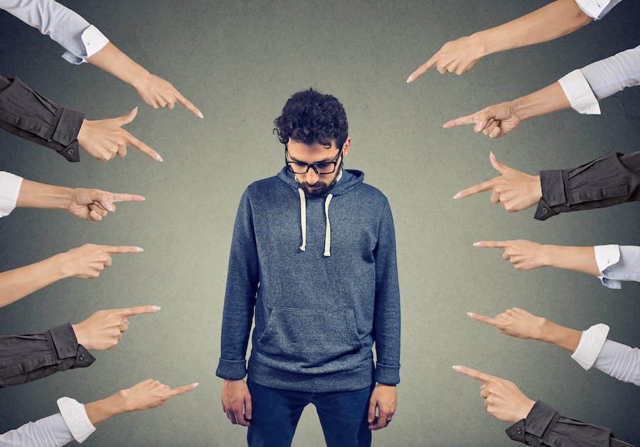 10 hands pointing accusatorily at a man looking down sheepishly