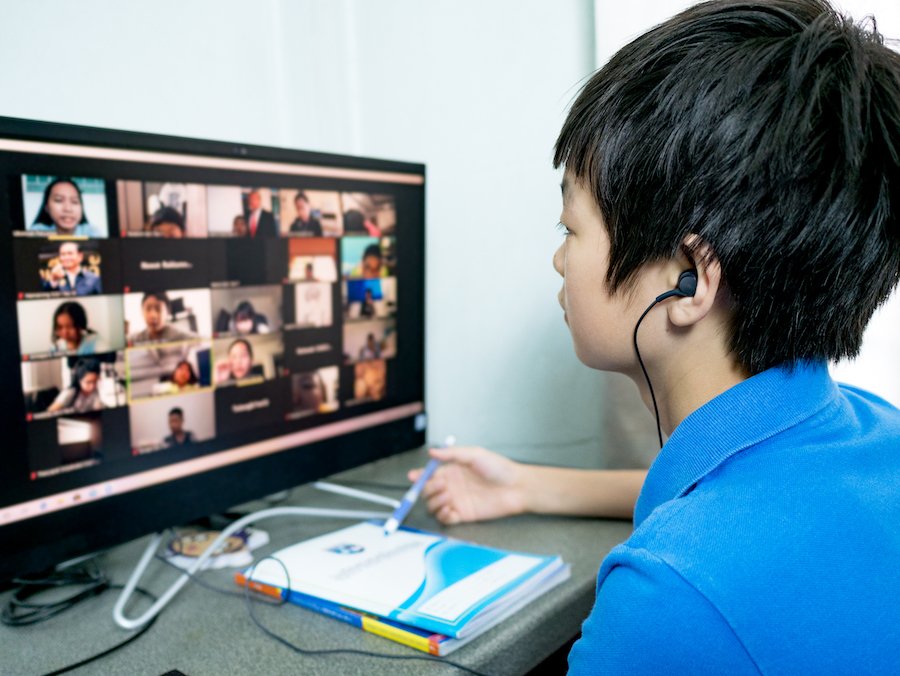 Young male student doing remote learning through his computer at a desk