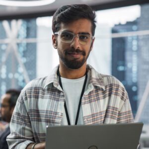 Man in glasses in front of a laptop in front of an office window, all suggesting he is a specialist in his trade