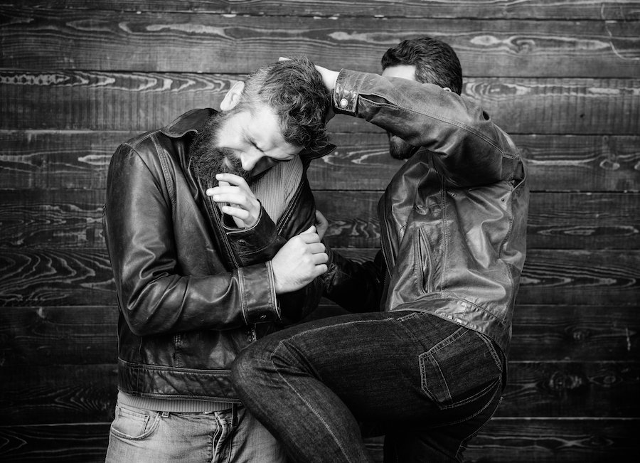 Foto en blanco y negro de dos hombres con chaquetas de cuero y jeans de mezclilla en una pelea a puñetazos contra una pared de madera Foto en blanco y negro de dos hombres con chaquetas de cuero y jeans de mezclilla en una pelea a puñetazos contra una pared de madera