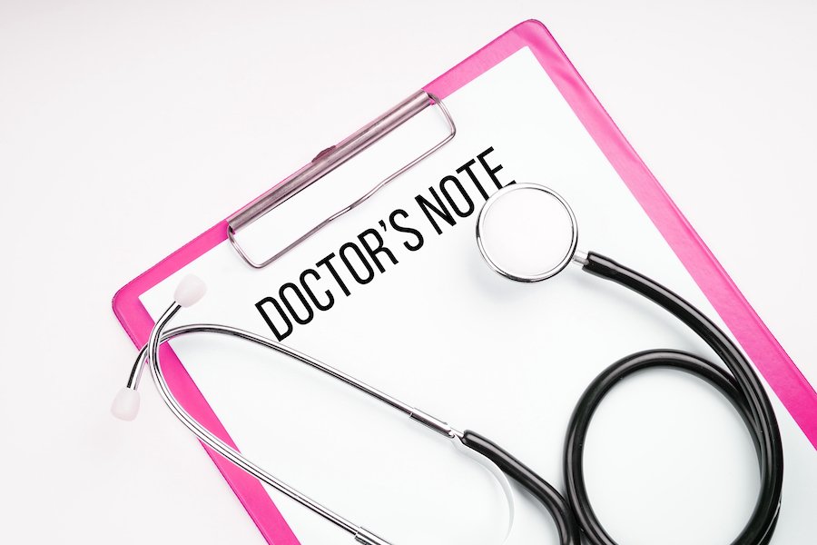 Pink clipboard with paper that says "doctor's note" underneath a stethoscope, against a white background