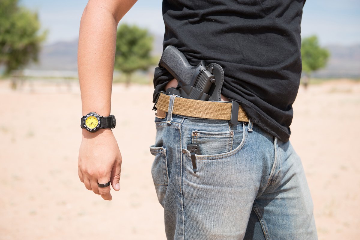 Man openly carrying a gun by tucking it into his waistband against a desert background