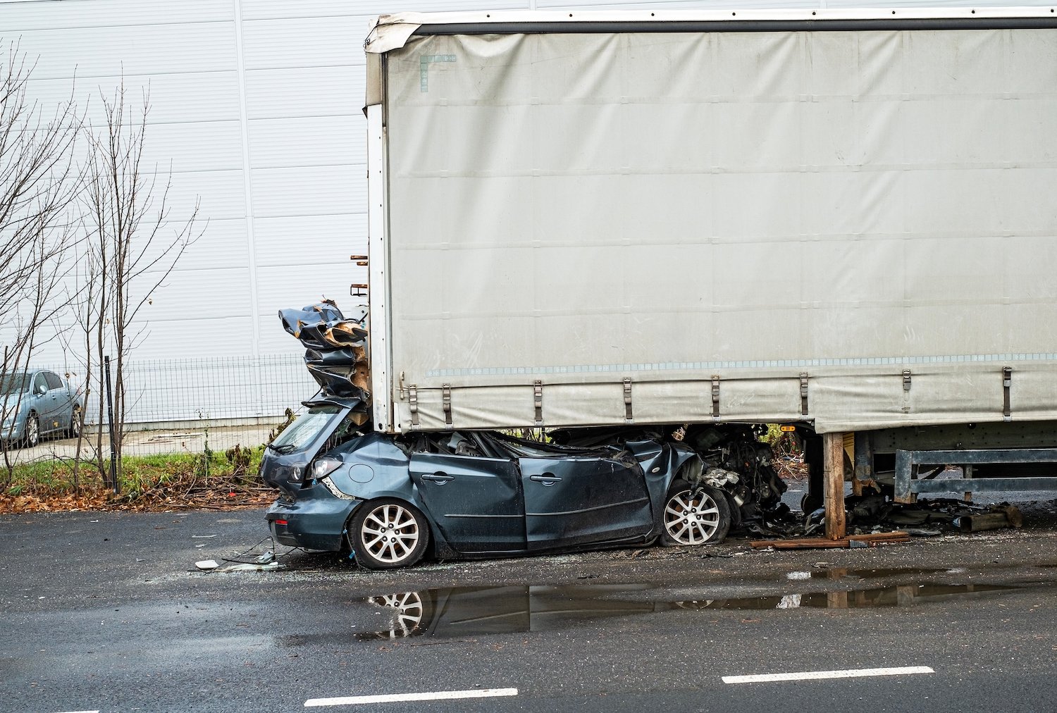 Sedán azul debajo de un camión blanco tras un choque en un día nublado