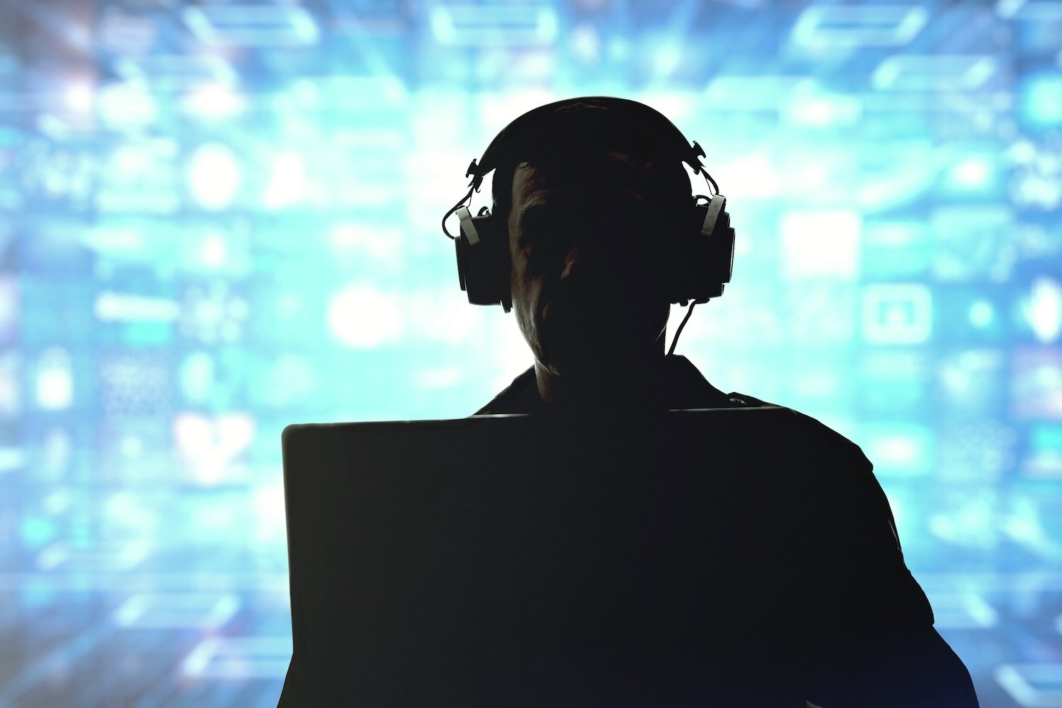 Silhouette of a man in headphones in front of a laptop while he is wiretapping a conversation