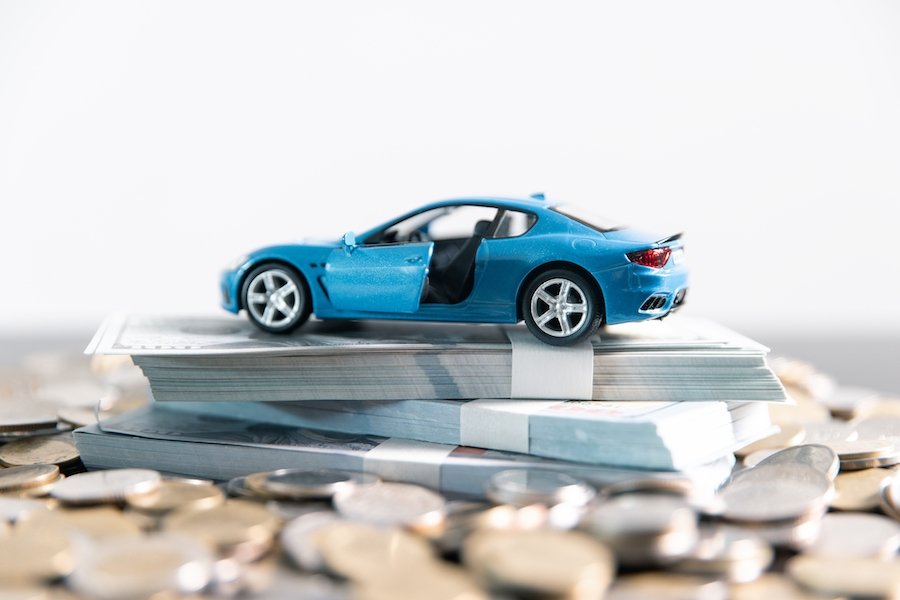Toy sports car on top of three wads of cash on top of a bed of coins