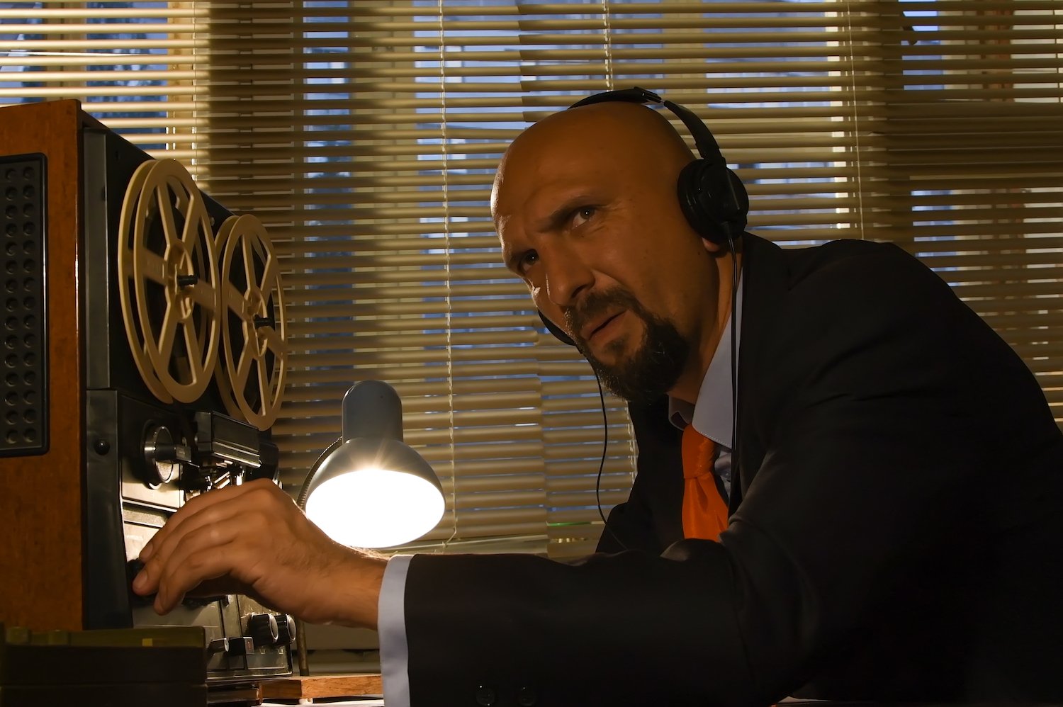 Man in headphones secretly wiretapping a phone call in a dark office