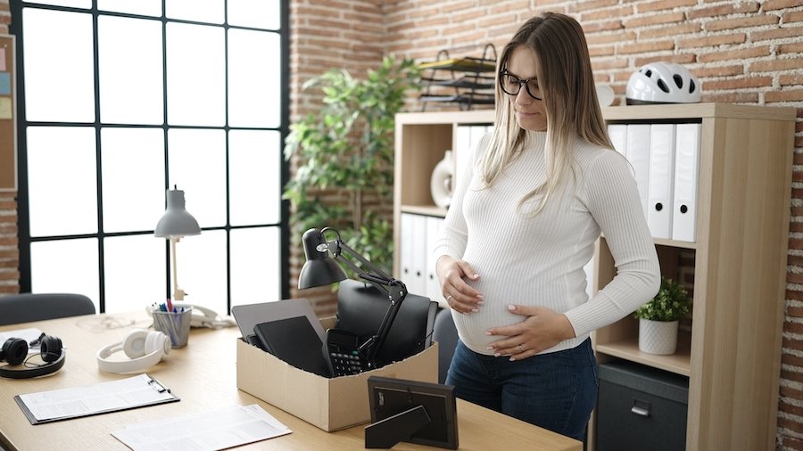 Mujer embarazada despedida Mujer embarazada con aspecto triste en una oficina de negocios empacando su escritorio después de ser despedida