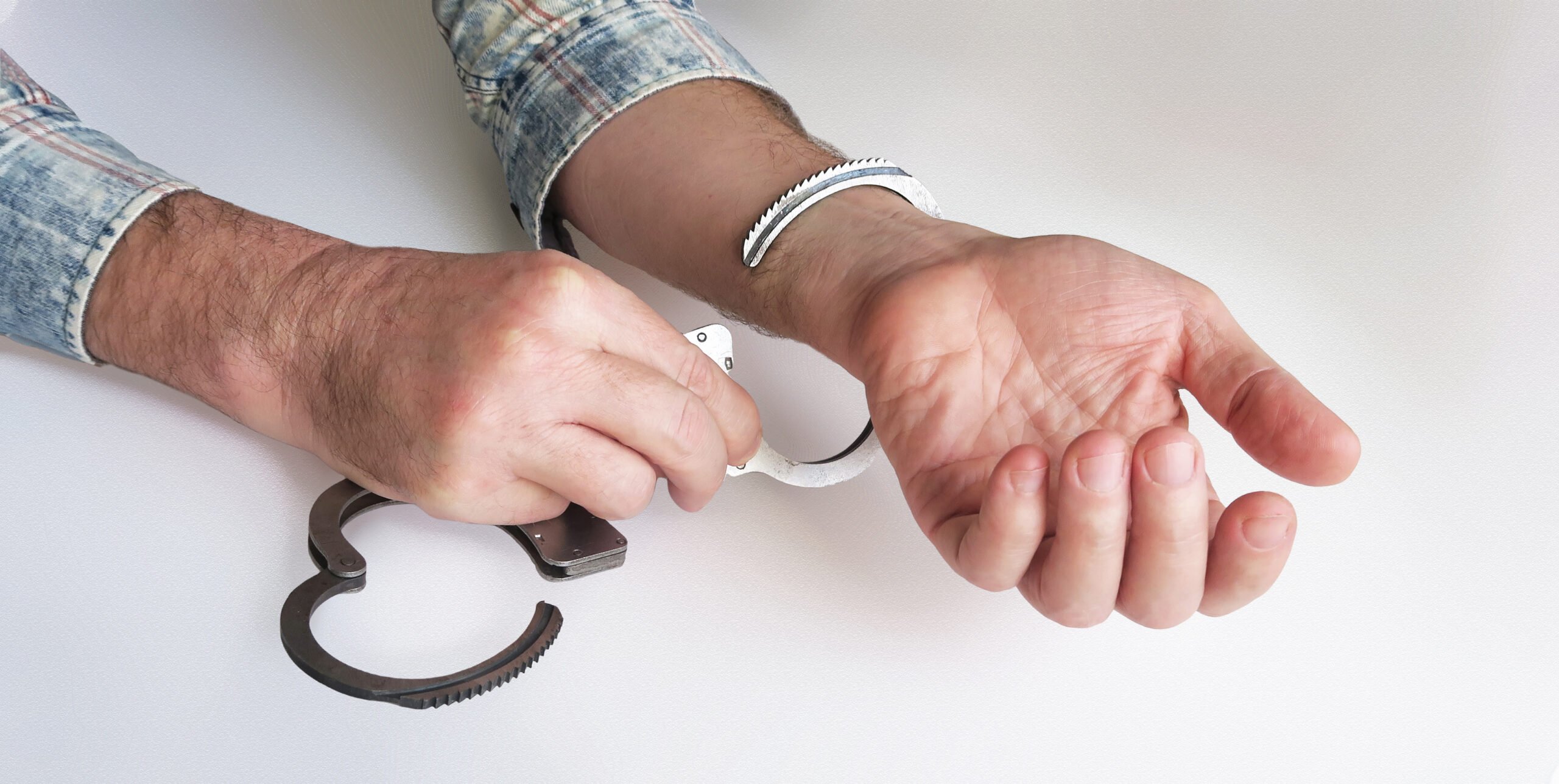 Closeup of two hands on a white table, and one hand is taking handcuffs off the other