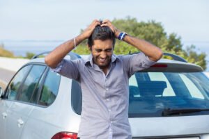 Hit and run victim holding his head in exasperation with his car in the background