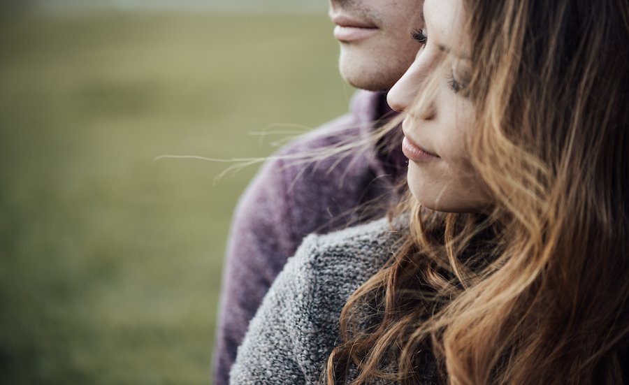 Closeup of young couple in love nuzzling against a grassy background