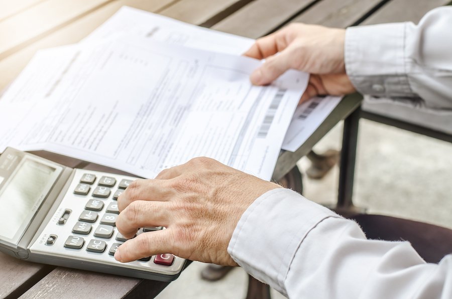 Closeup of a person's hand on calculator and the other hand holding a wage statement on a desk