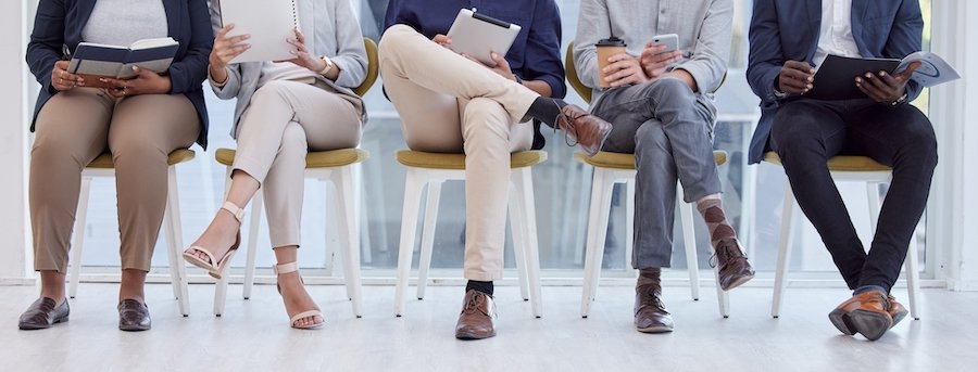 Row of sitting job applicants waiting to be interviewed against a floor to ceiling office window