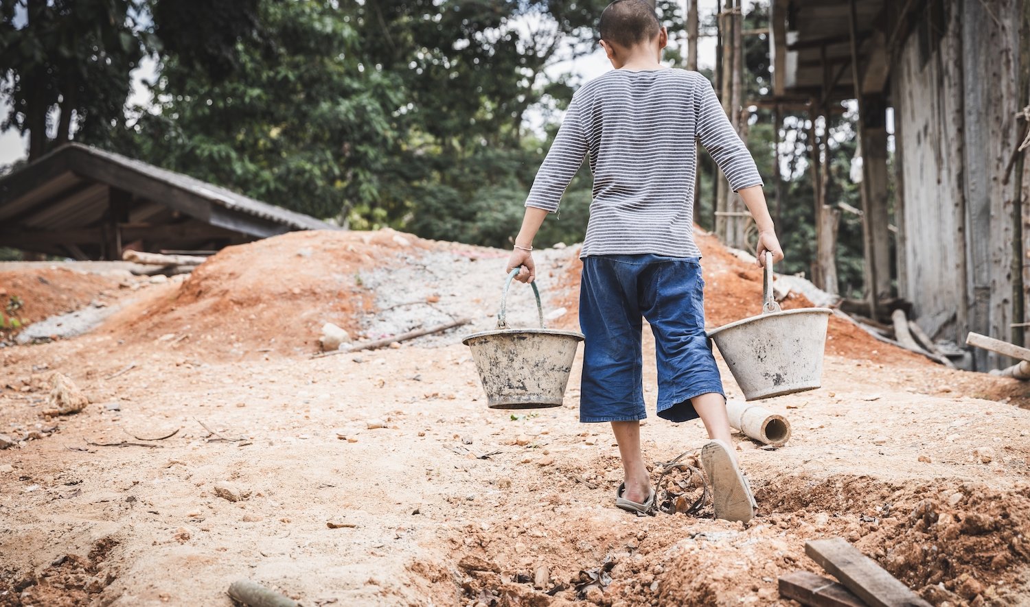 Young child holding buckets of dirt on a worksite