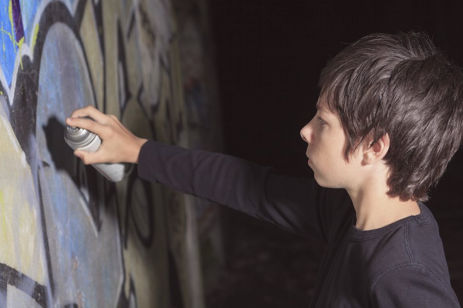 Young boy at night spray-painting a wall in an act of vandalism
