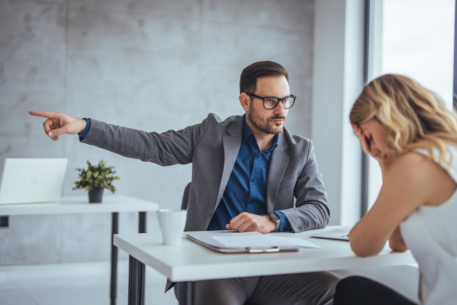 Male employer firing a female worker in an office, and he is pointing her to towards the door