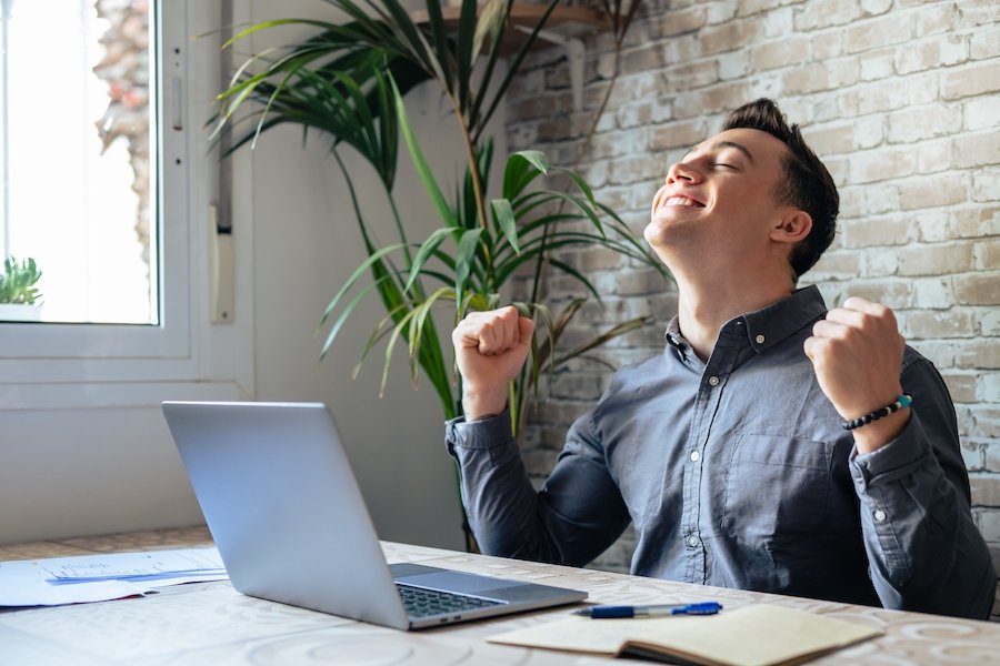 Young man pumping his fist in happiness after receiving a job offer on his laptop computer