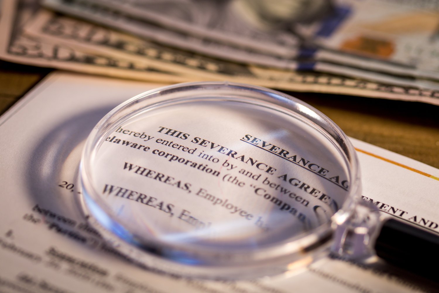 Magnifying glass over a severance agreement on a desk