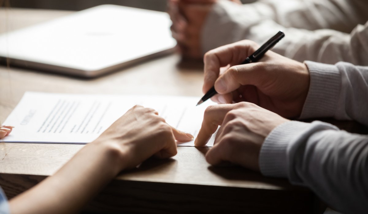 Man signing a severance agreement on a desk while he is surrounded by two people advising him